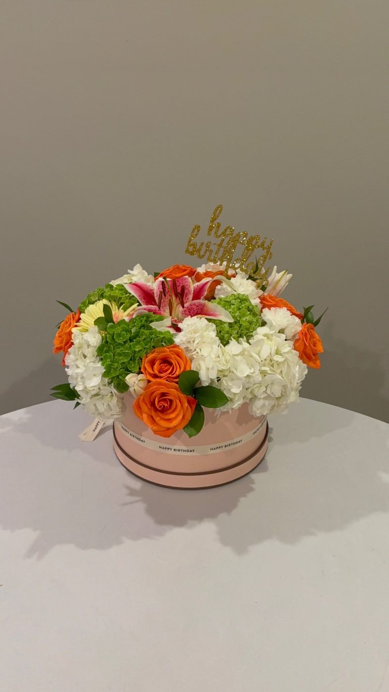 Birthday hatbox of orange roses, stargazer lily, hydrangea and bells of Ireland with a Happy Birthday topper
