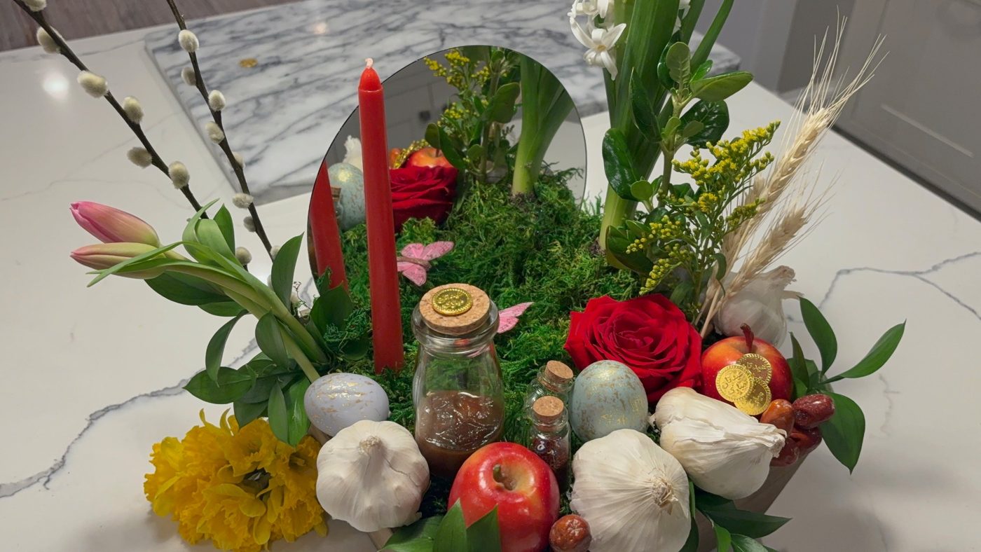 Nowruz haft-sin centerpiece with a mirror, red candle, moss, hyacinth, wheat, apples, garlic, painted eggs and gold coins