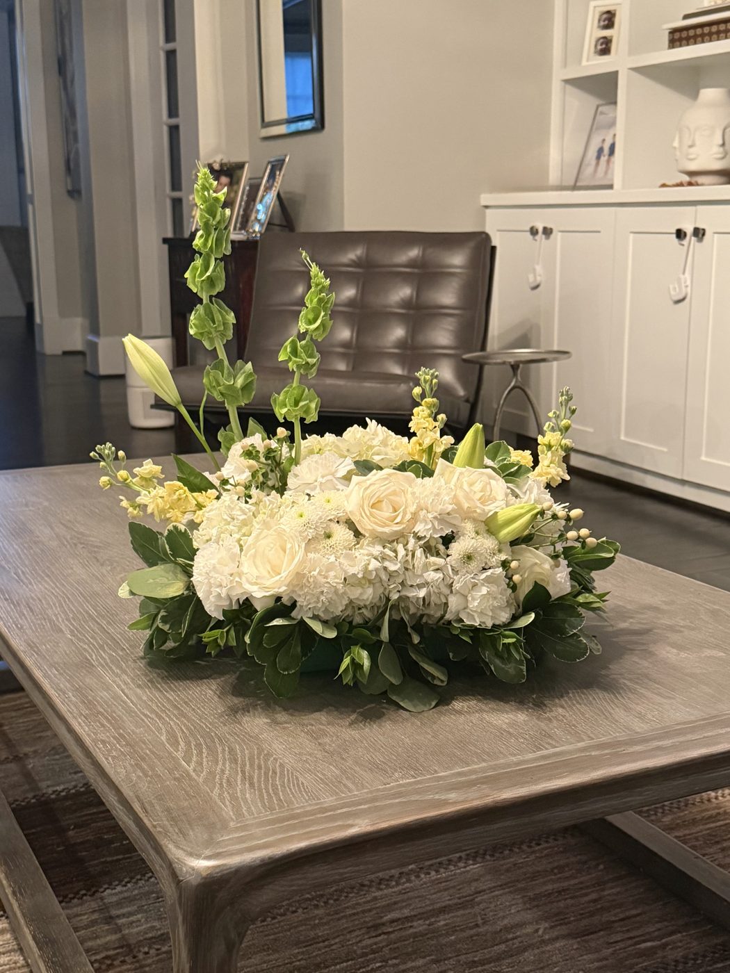White and green centerpiece of roses, hydrangea, lilies, stock and bells of Ireland
