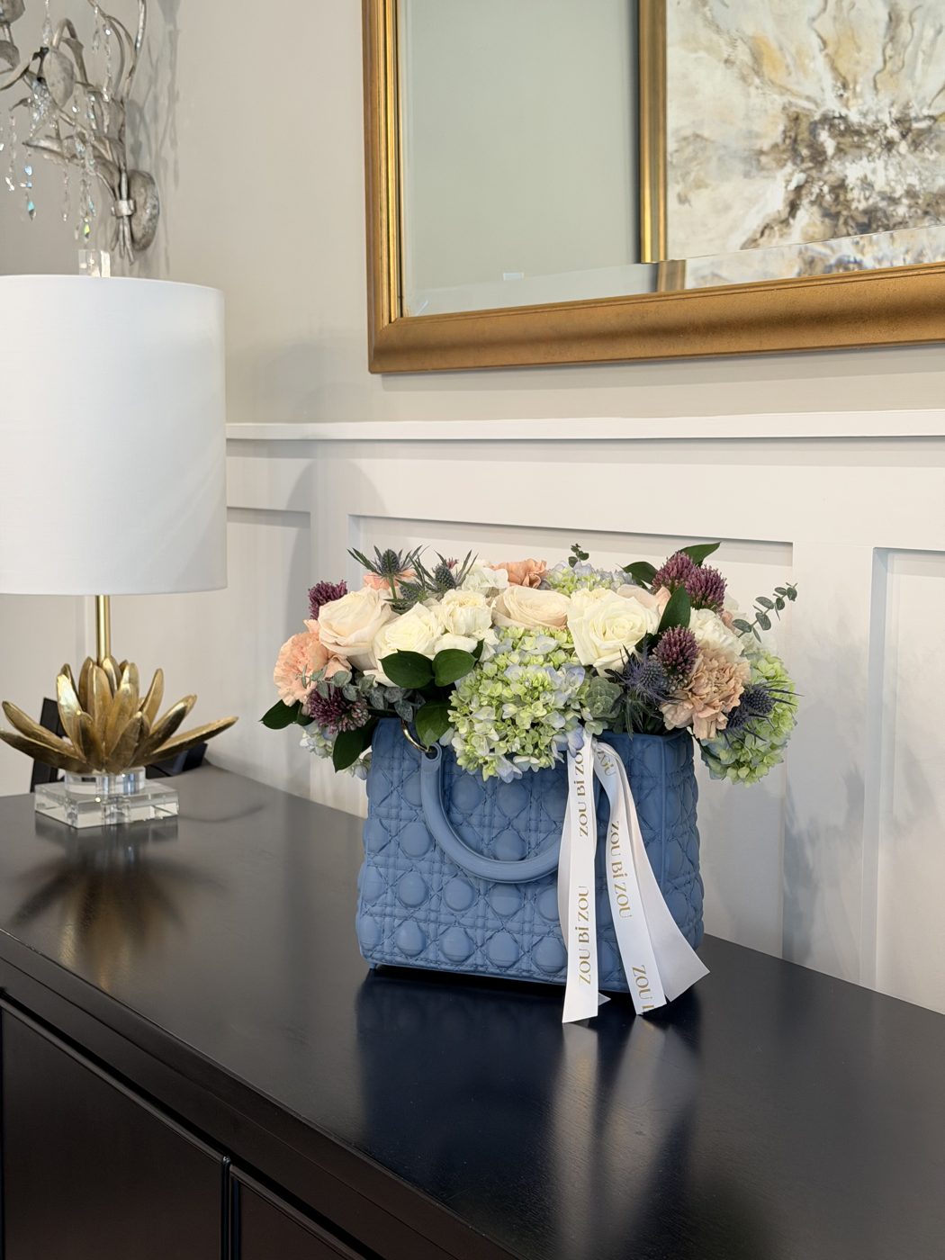 Blue quilted handbag-style vase of cream roses, peach carnations, hydrangea, thistle and allium with Zou Bi Zou ribbons