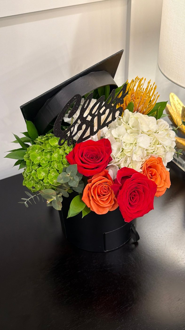 Graduation-cap hatbox of red and orange roses, hydrangea, pincushion protea and a Class of 2026 topper