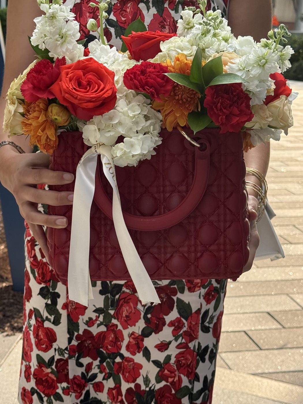 Red quilted handbag-style arrangement of orange roses, red carnations, dahlias, stock and hydrangea