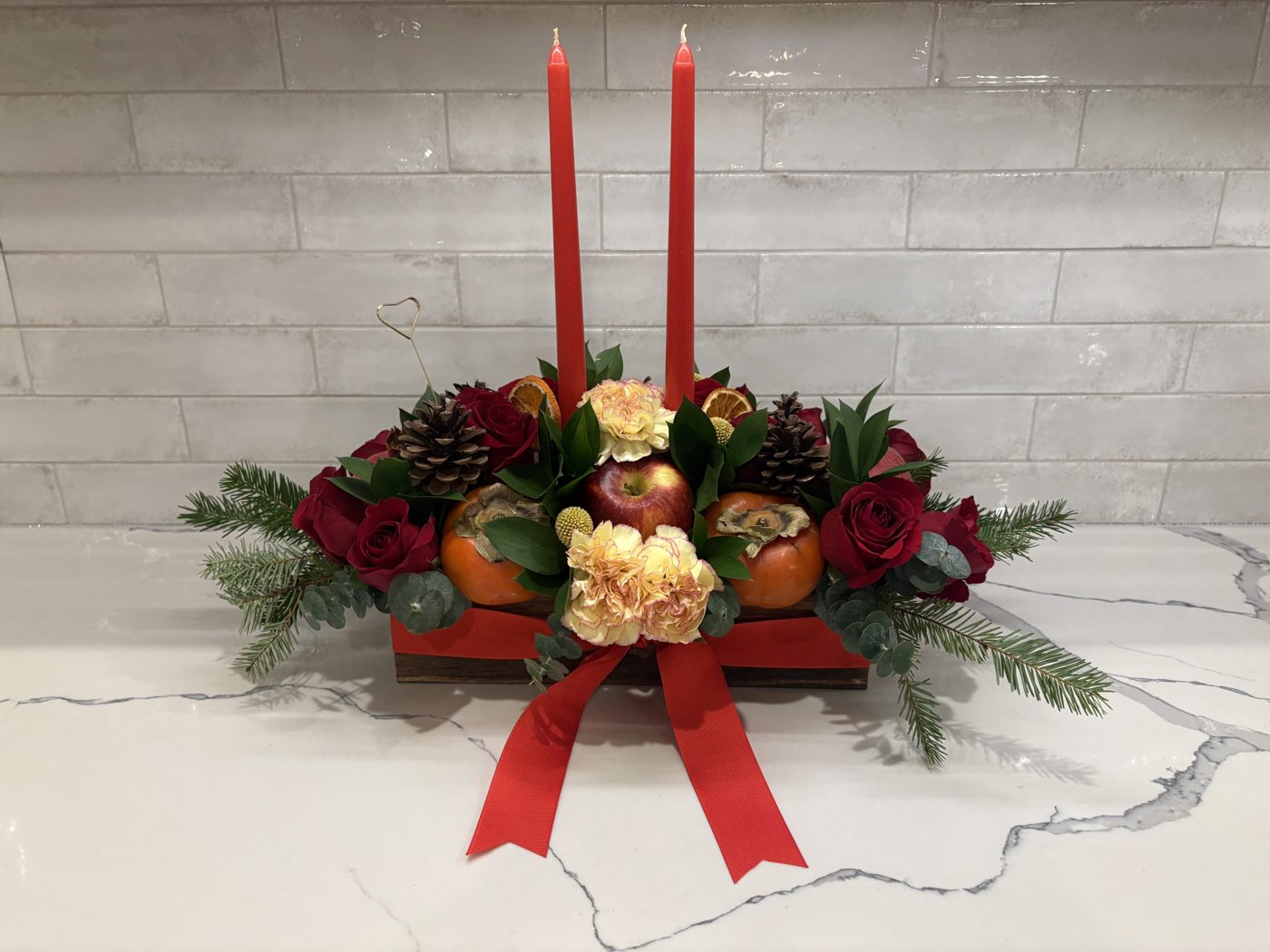 Holiday table centerpiece with red roses, pinecones, greenery and red taper candles