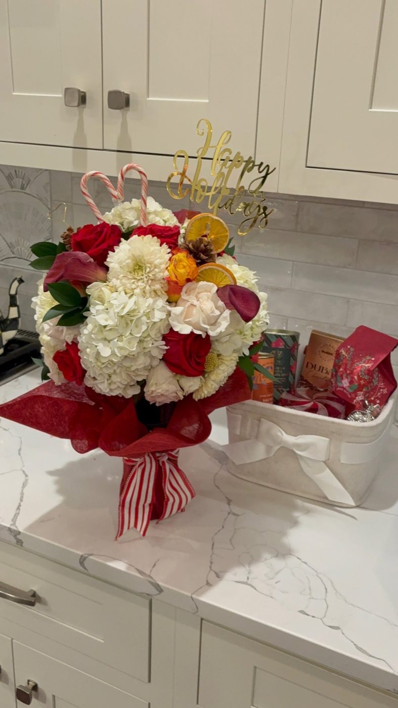 Holiday bouquet of hydrangea, roses and calla lilies with candy canes and a Happy Holidays topper, beside a matching gift basket