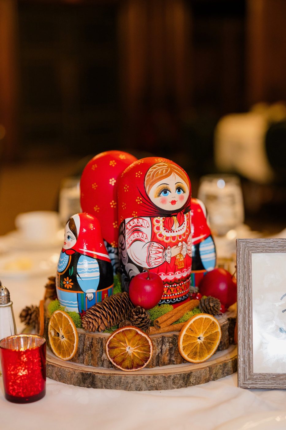 Table centerpiece of painted nesting dolls with dried oranges, pinecones and apples on a wood slice